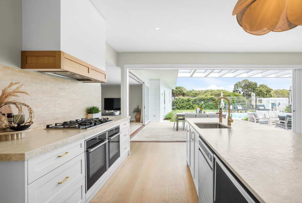 A modern kitchen with cabinetry, a marble island countertop, and pendant lighting, highlighted by an open-plan layout and wooden flooring that adds warmth to the contemporary space.